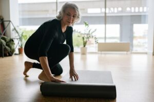 Lady with a yoga mat crouching about to exercise.