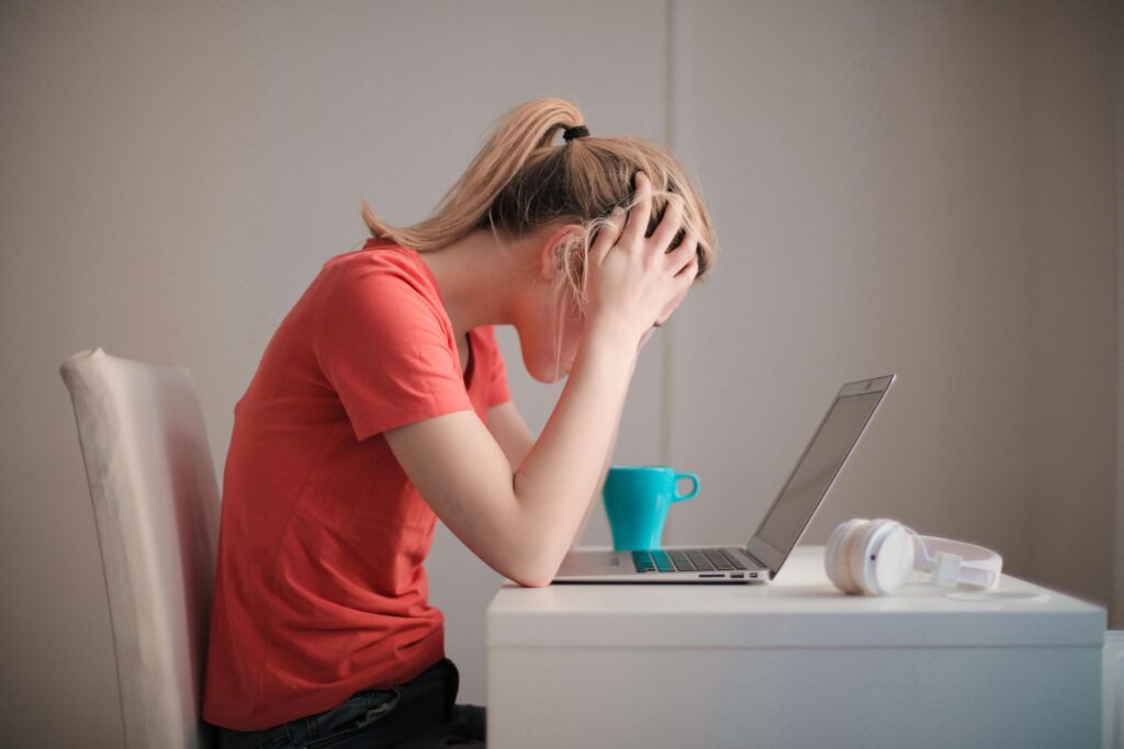 Woman at a desk holding her head, representing modern stress and mental overload.