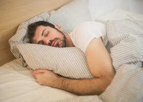 Man sleeping peacefully on striped bedding, embracing relaxation and comfort.