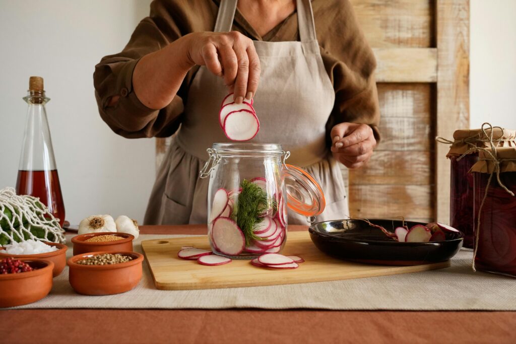 A woman preparing pickled radishes, showing fermented foods and colourful plants in a rustic kitchen.