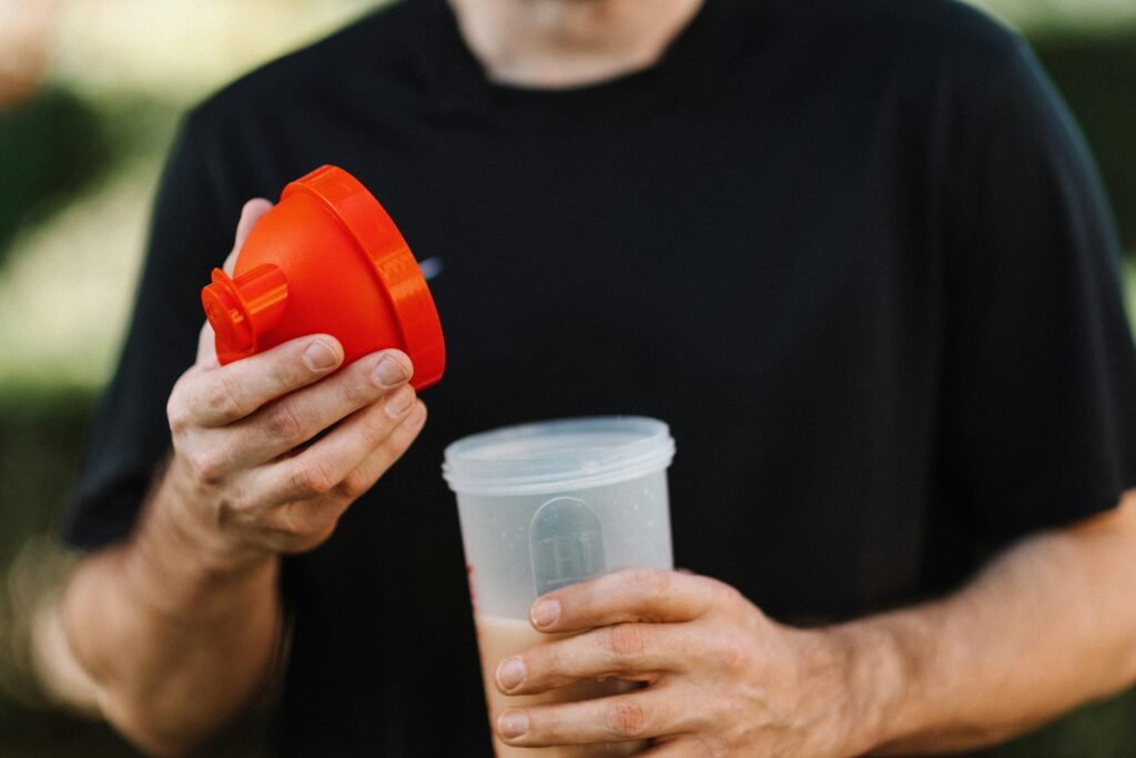 A man in a black shirt holding a protein shake outdoors.